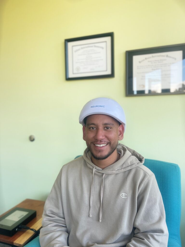 Client smiling while wearing the Neuronic PBM light therapy helmet at Healthy Within in San Diego