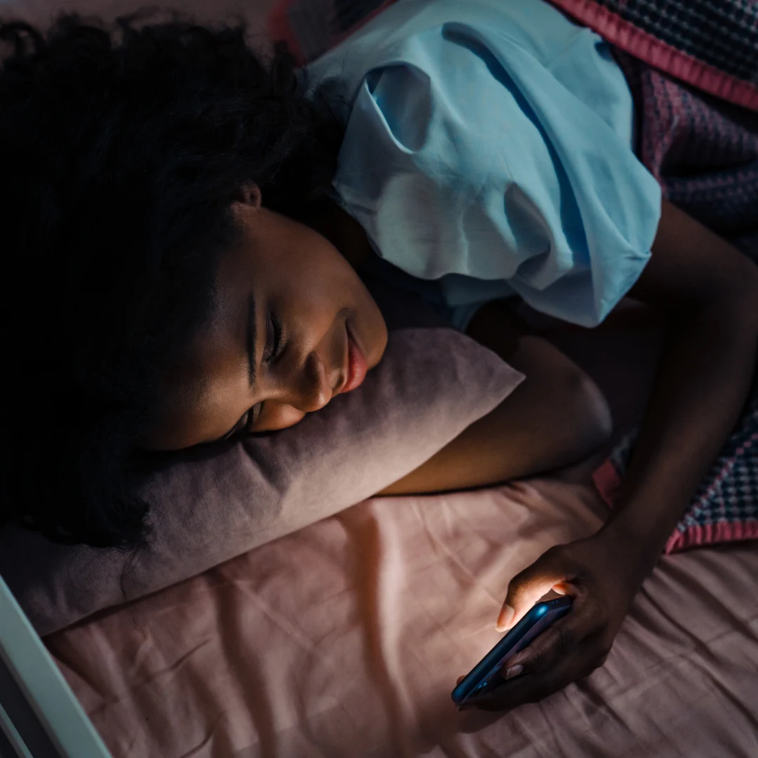 Person lying in bed at night lit by the glow of a phone screen, illustrating late-night screen time and disrupted focus